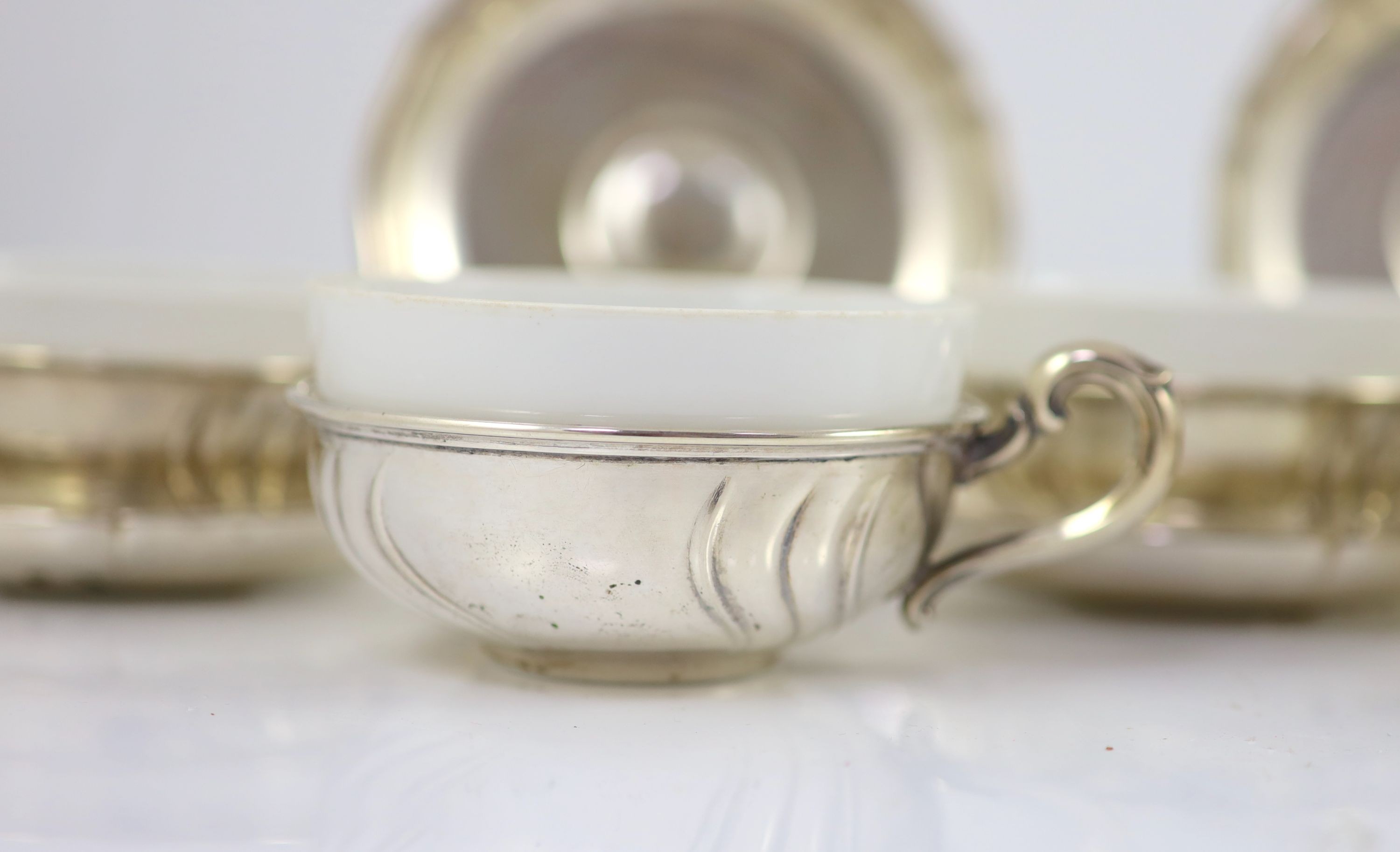 A set of eight German 800 standard silver cups and saucers, by Adolf Kander, with white porcelain liners